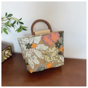 Dettaglio della borsa in lino con ricamo floreale di paillettes e manico in legno