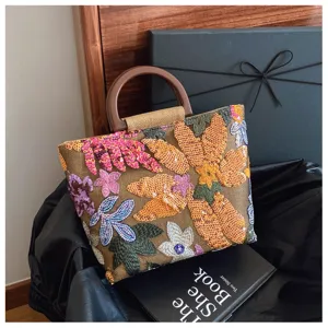 Dettaglio della borsa in lino con ricami floreali di paillettes e manico in legno.