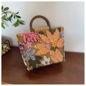 Vista dettagliata del ricamo floreale su una borsa a mano in lino con manico in legno.