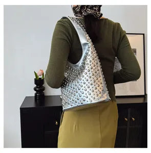 Stylish silver bucket bag with metal studs worn as a shoulder bag on a green sweater.