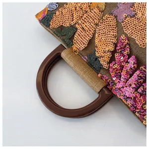 Primo piano dei motivi floreali in paillettes e del manico tondo su una borsa di lino