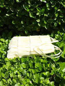 Close-up view of a cream-colored layered ruffled pleated tote bag placed on green leaves