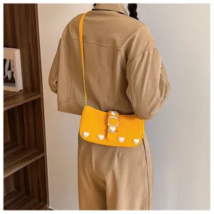 Yellow baguette shoulder bag with sweet pearl heart decorations worn by a model