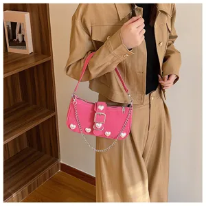 Close-up of a pink baguette bag with heart pearl accents and a metallic chain strap
