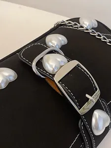 Chic black baguette bag featuring large heart-shaped pearl studs and silver chain strap