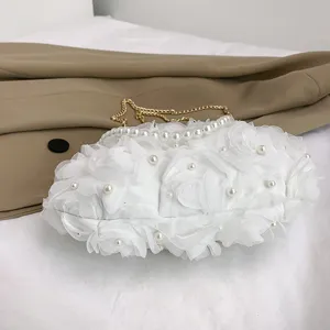 Vue détaillée des roses en tissu blanc et des perles sur un sac de soirée design.