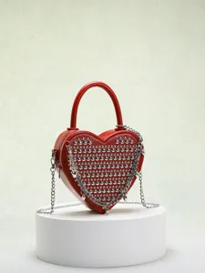 Detail shot of the red heart-shaped studded crossbody bag featuring metallic chain and silver rivets.