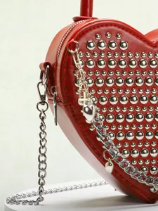 Red heart-shaped crossbody bag with silver studs and metal chain detail, fashion detail shot.