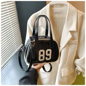 Detail of a black patent leather bowling handbag featuring white '89' and piping.