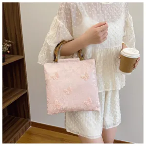 Detail of pink embroidered butterfly handbag with natural bamboo top handles