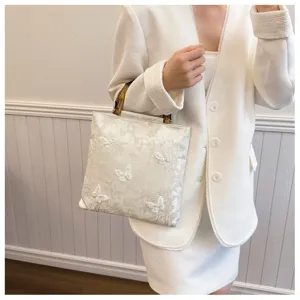 Detail view of elegant white evening bag with butterfly embroidery and bamboo handle