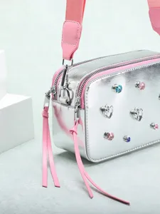 Bolso de cámara plateado metalizado con correa rosa y pedrería en forma de corazón
