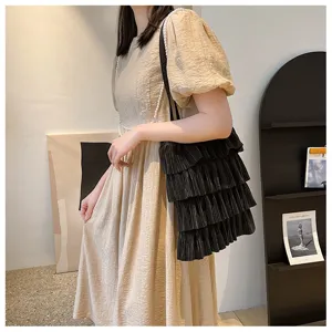 Seitenansicht einer schwarzen gestuften Plissee-Tasche mit Perlenriemen am Model