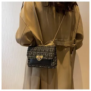Close-up detail of black tweed crossbody bag with gold chain strap on shoulder