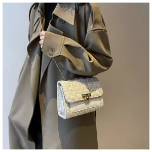 Close-up of elegant tweed crossbody bag with gold chain strap worn with a trench coat