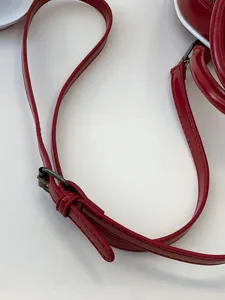 Close-up of red oil skin shoulder strap with dark metal buckle on fashion bowling bag.