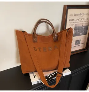 Detail view of casual brown corduroy tote bag with leather handles and stylish embroidered text.