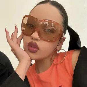 Close-up view of oversized orange Y2K wrap-around sunglasses worn by a stylish model