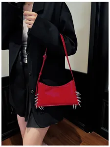 Close-up of red patent leather shoulder bag with punk metal rings, underarm style detail.