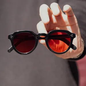Primer plano de gafas de sol redondas negras con lentes rojas y remaches clásicos