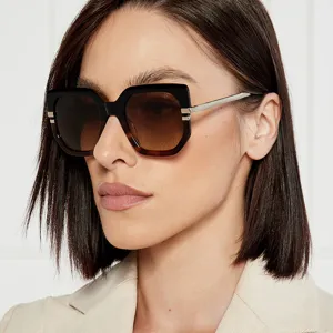 Close-up of woman wearing oversized irregular sunglasses with brown gradient lenses