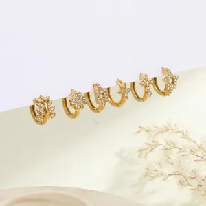 Detail of gold-plated stainless steel huggie earrings with leaf, star and cross charms.
