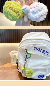 Close-up detail of plush tennis ball and baseball keychains on a white backpack