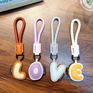 Set of four colorful PU leather alphabet keychains spelling LOVE on a rustic wood background