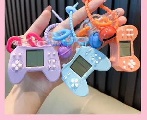 Close-up of three mini retro handheld game console keychains in pastel colors held in a hand