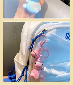 Detail view of a pink iridescent unicorn keychain hanging on a white canvas backpack