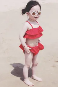 Toddler girl wearing cute flower-shaped white sunglasses on a sandy summer beach