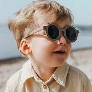 Niño con elegantes gafas de sol redondas con protección UV en la playa bajo el sol