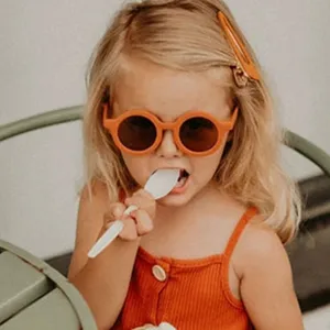 Niña a la moda con elegantes gafas de sol redondas de color naranja para niños protección UV.