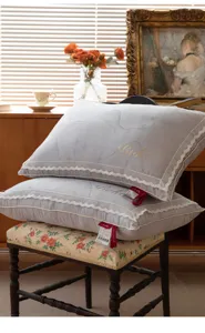 Detail of elegant grey pillow with lace trim and gold embroidery in a cozy room.