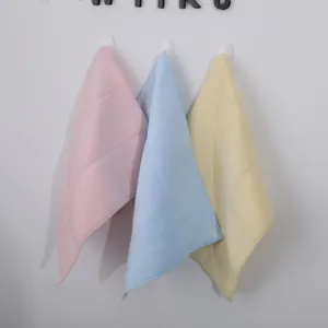 Three soft latex square face towels in pink, blue and yellow hanging on white wall
