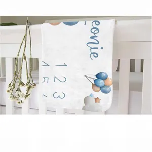Soft baby monthly milestone blanket with blue balloons draped over a white wooden crib