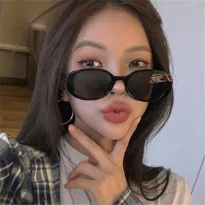 Una vista detallada de gafas de sol ovaladas retro con montura negra en una modelo