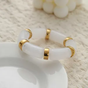 Gros plan d'un bracelet en acrylique blanc avec des anneaux dorés sur une assiette en céramique.