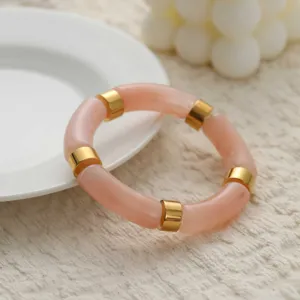 Détail d'un jonc en résine marbrée rose avec des accents métalliques dorés sur une assiette