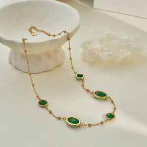 Detail of stainless steel necklace with green oval gemstones and gold bead chain