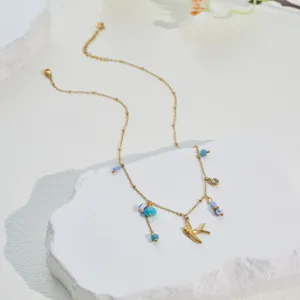 Detail shot of a gold bird pendant necklace with turquoise and blue enamel beads.