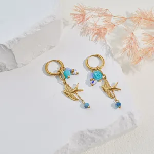 Close-up of golden stainless steel hoop earrings with bird and blue rose charms