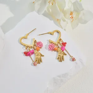 Close-up of stainless steel heart earrings with colorful beads and pink flower charms.