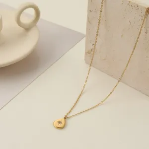 Primer plano de un collar de acero inoxidable dorado con colgante de gota grabado con estrella