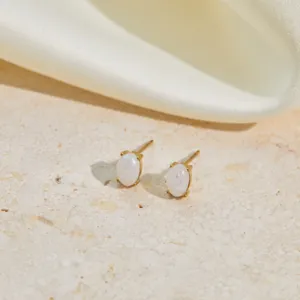 Close-up of elegant oval white opal stud earrings on a textured stone surface