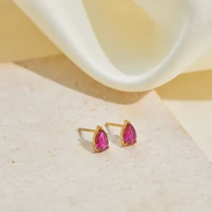 Close-up of gold stainless steel stud earrings with pear-shaped pink birthstone.