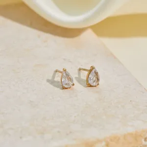 Detailed macro shot of elegant pear-shaped clear zircon gold stud earrings on stone