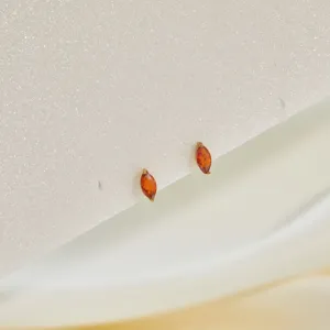 Detailed macro view of marquise-cut orange cubic zirconia stud earrings on white glitter card