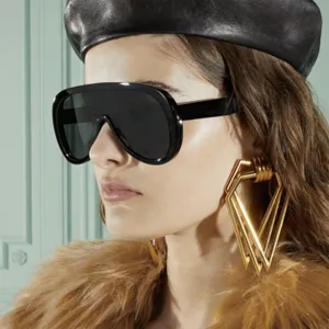 Close-up of oversized black shield sunglasses on model with fashion accessories