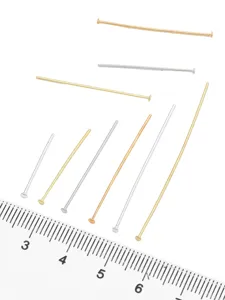 Close-up of metal T-pins in various colors next to a ruler for scale measurement